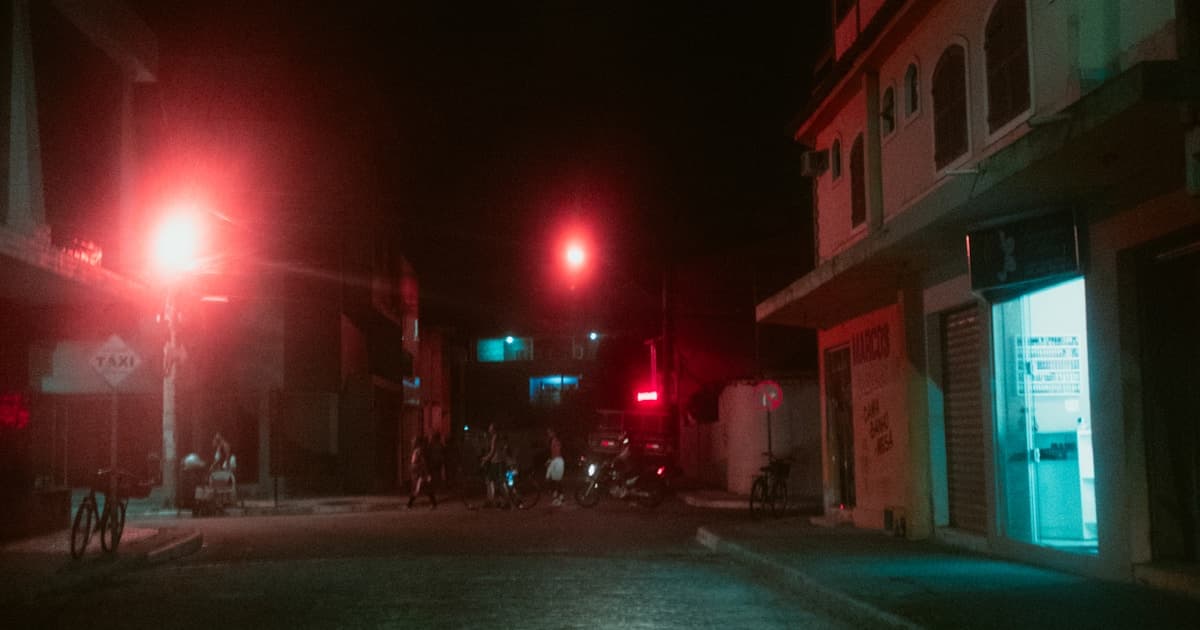 Rua brasileira à noite com iluminação vermelha e pessoas nas sombras — o lado sombrio do carnaval