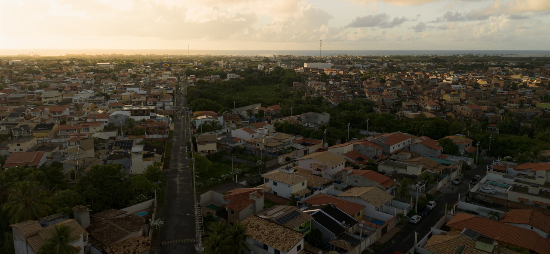 Vista aérea de cidade brasileira ao pôr do sol com bairros populares e ruas sinuosas